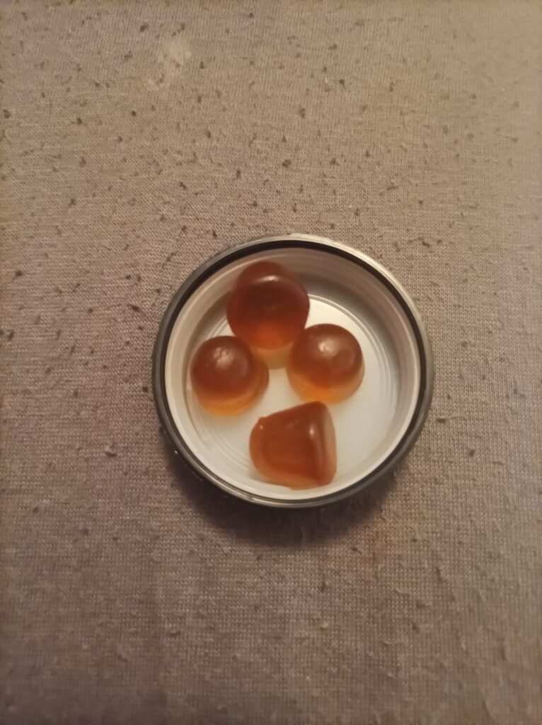 Quatre gummies de compléments alimentaires, posés dans le bouchon du flacon.