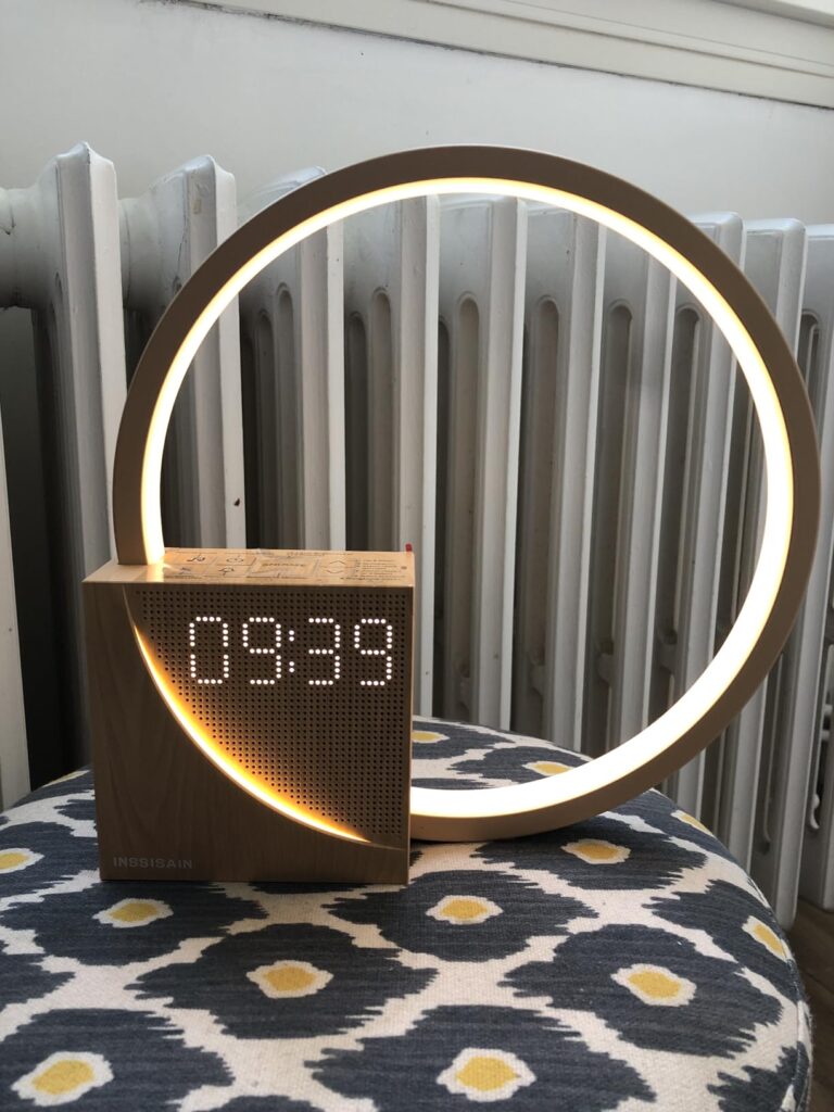 Le réveil-lampe est posé sur un tabouret, la lumière est allumée et l'heure est affichée. L'image montre la base du réveil-la...