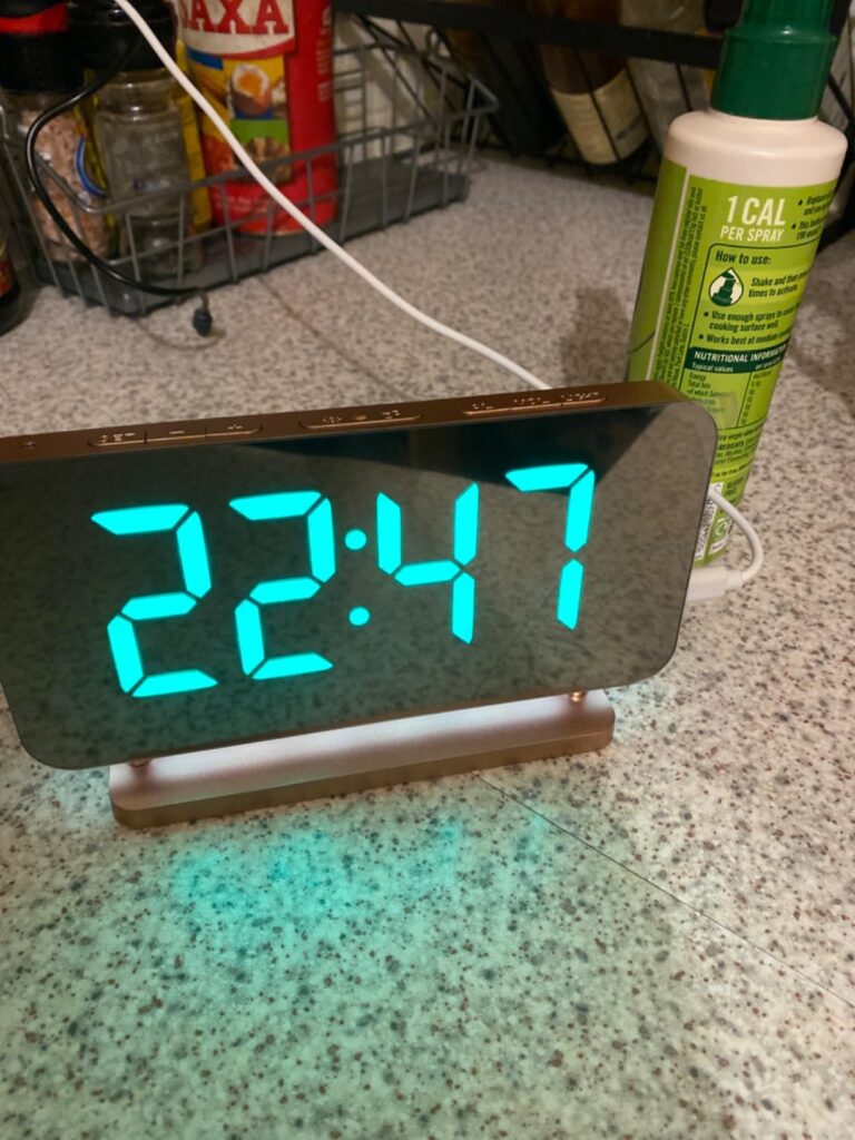 Réveil posé sur une surface, affichant l'heure. La base est vert pâle.