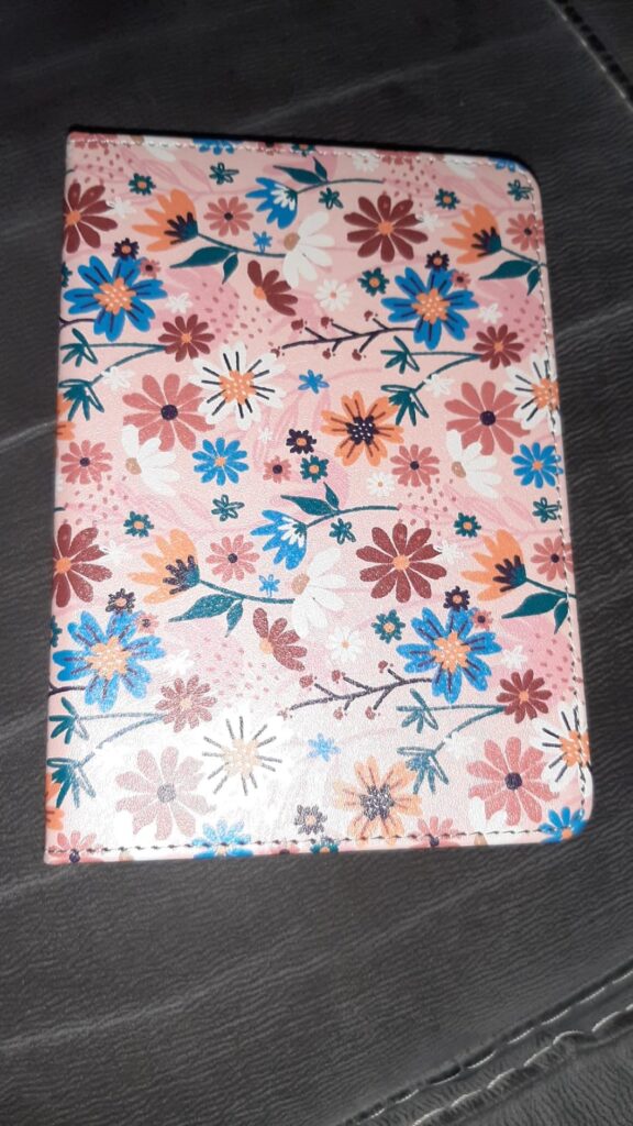 L'étui de liseuse est posé sur une surface sombre, montrant un motif floral rose et bleu.