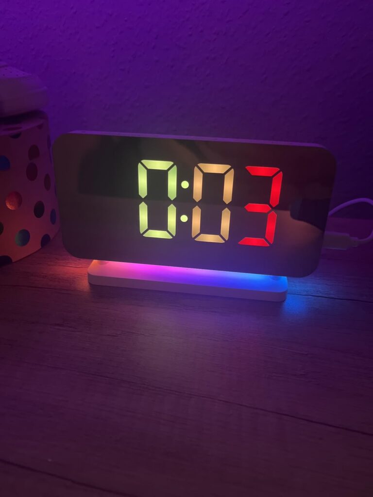 L'horloge-réveil dans l'obscurité, affichant l'heure en différentes couleurs.