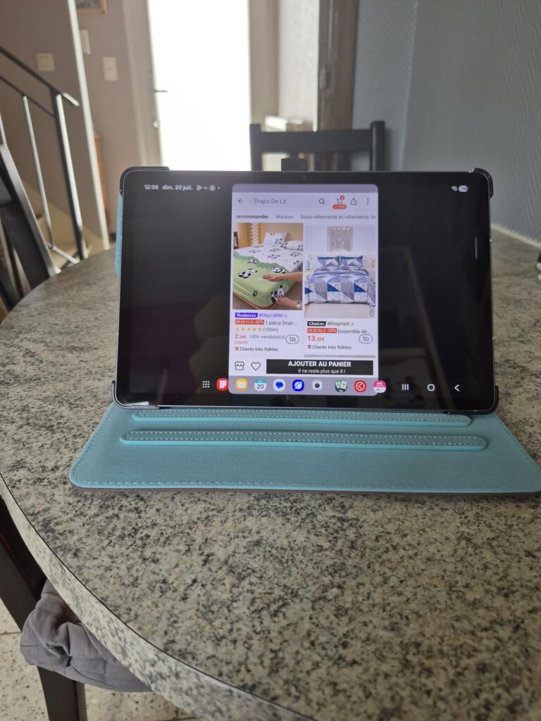 Vue d'une tablette dans sa coque bleu clair posée sur une table, affichant une application.