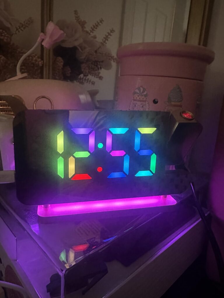 Réveil en gros plan, affichant l'heure 12:55 avec des chiffres multicolores, et un éclairage d'ambiance violet.
