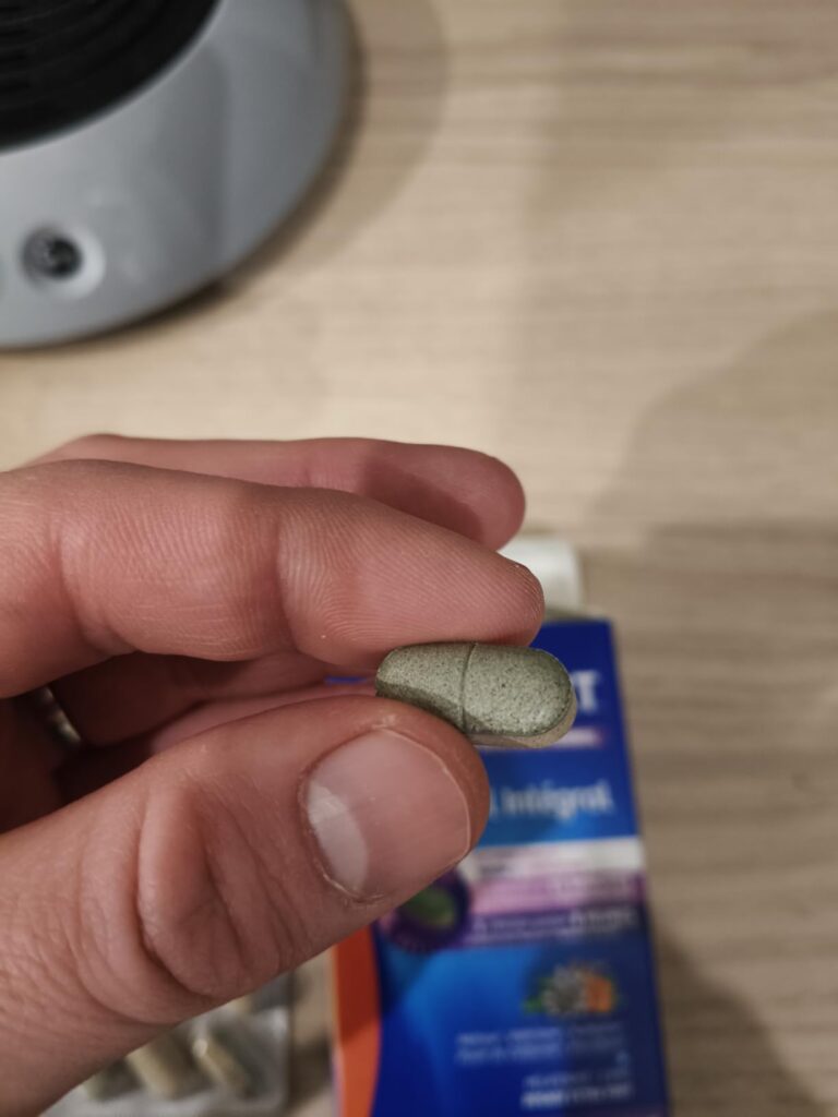Un comprimé bicouche tenu entre deux doigts, avec la boîte de Valdispert en arrière-plan.