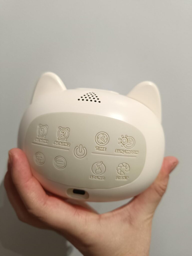 Vue arrière du réveil en forme de chat tenu dans une main, montrant les boutons de réglage et le port de charge.