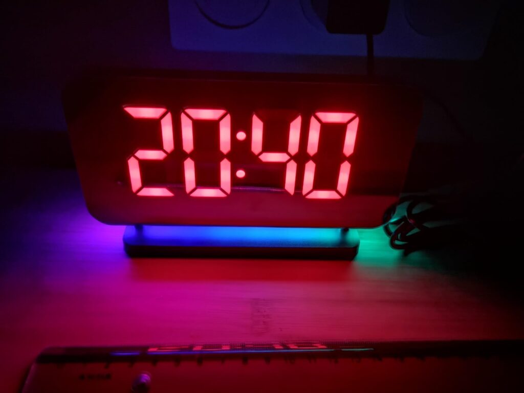 Gros plan sur le radio-réveil. L'affichage est rouge. La lumière d'ambiance à la base est multicolore.