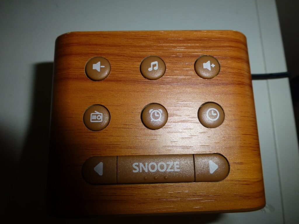 Gros plan sur le dessus du réveil, montrant les boutons de réglage et le bouton snooze. Le réveil est en bois clair.