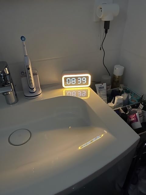 Le réveil sur un lavabo de salle de bain. La lumière est jaune. Il est branché au mur.