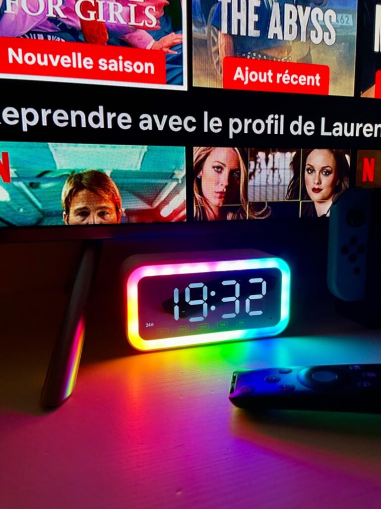 Le réveil sur une table, reflétant sa lumière sur le mur, avec un écran de télévision en arrière-plan. La lumière émise par l...