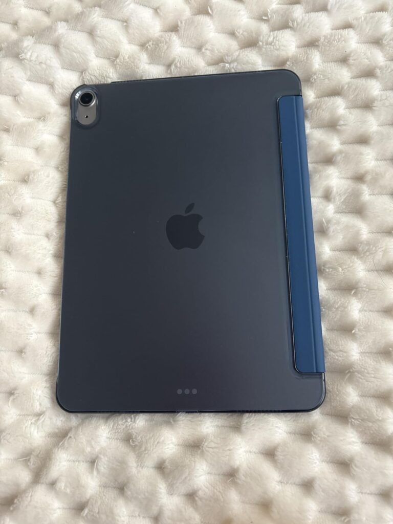 Vue de dos de la tablette iPad Mini 6 de couleur grise sidérale, avec sa coque de protection bleue sur un plaid blanc et moel...