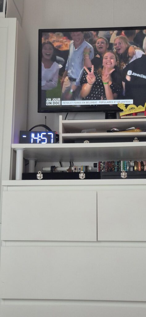 Le réveil est visible sur un meuble sous une télévision, l'heure est affichée en blanc.