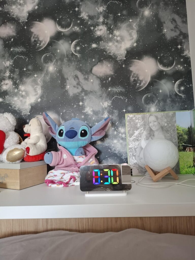 Le réveil posé sur une étagère à côté d'une peluche Stitch et d'une photo.