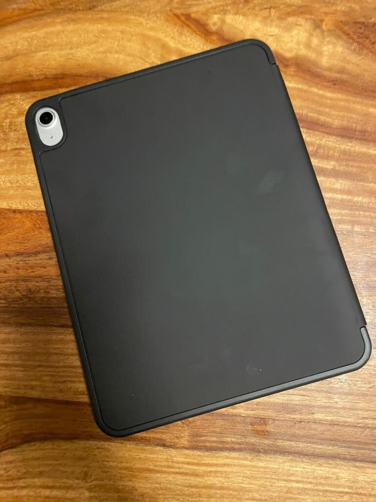 Vue arrière de l'iPad avec une coque noire, posé sur une table en bois. Le module caméra est visible dans le coin supérieur g...
