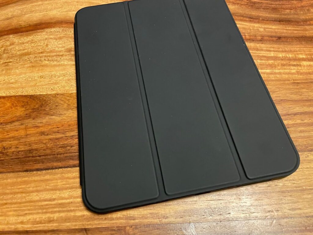 Vue de dessus de l'iPad avec son étui folio noir fermé, posé sur une table en bois. La partie avant de l'étui est visible, mo...
