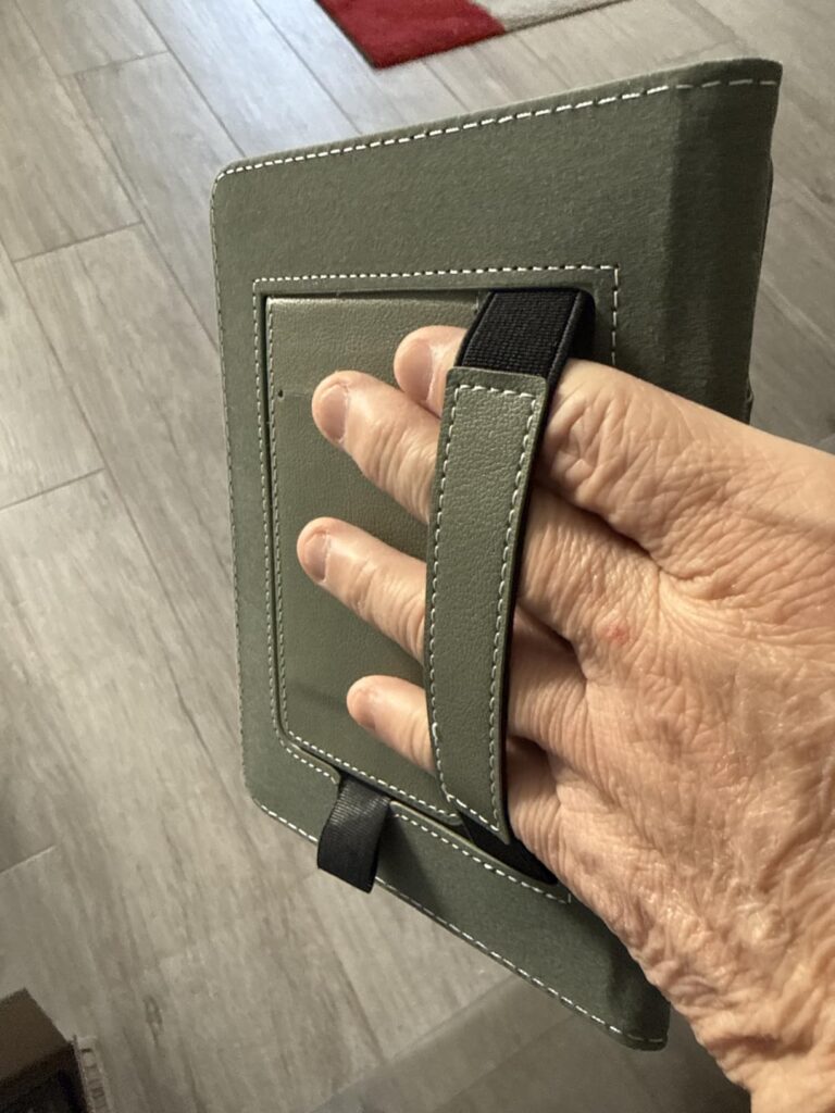 Gros plan sur une main tenant la liseuse à l'arrière, montrant la lanière de maintien.