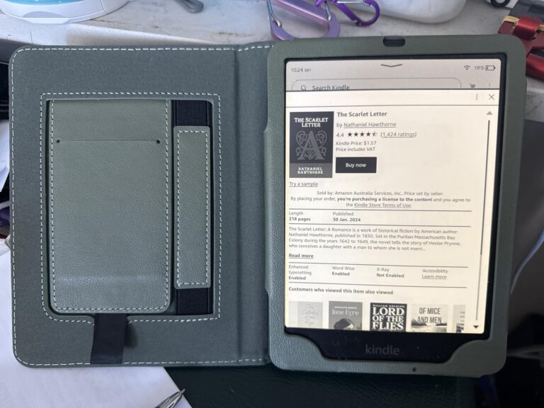 Liseuse dans son étui ouvert, posée sur une table, écran affichant une page produit Amazon pour un livre.