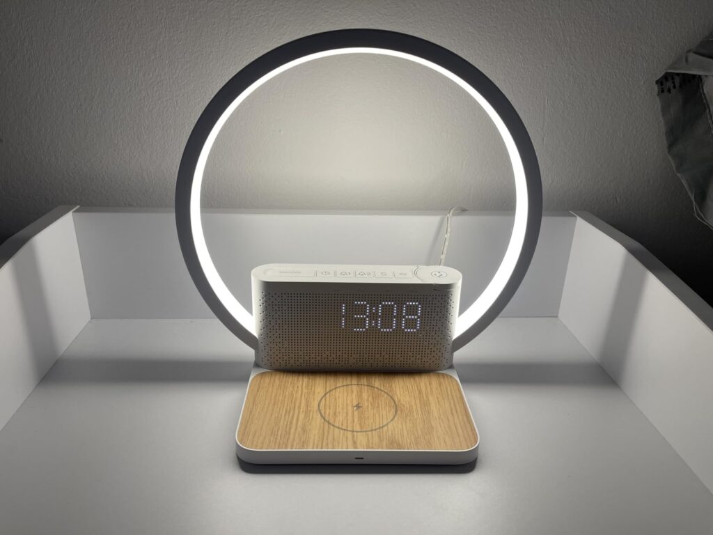 Réveil-chargeur avec lampe d'ambiance allumée, posé sur une étagère, devant un mur clair.