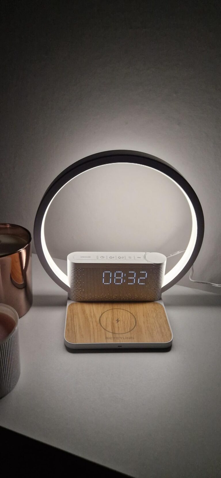 Réveil-chargeur avec lampe d'ambiance allumée, posé sur une surface sombre, devant un mur clair.