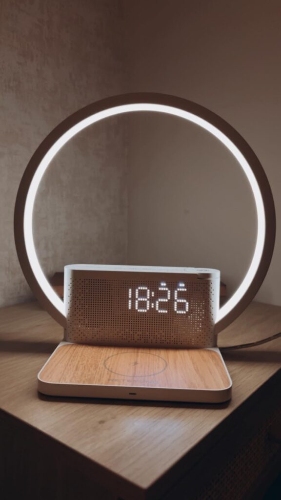 Réveil-chargeur avec lampe d'ambiance allumée, posé sur une surface en bois, devant un mur clair.