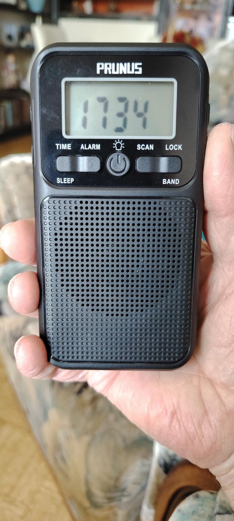 Le poste de radio tenu dans une main, l'écran affiche l'heure.