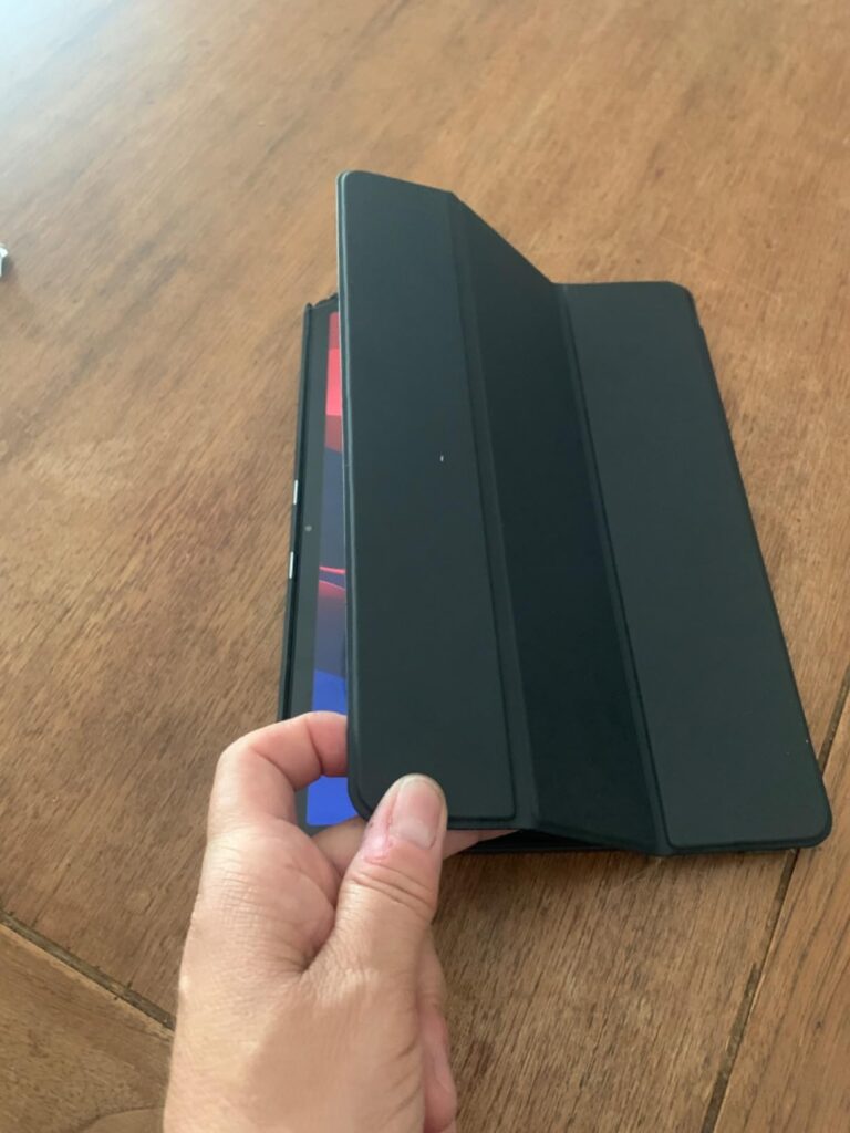 La tablette avec une coque de protection noire est posée sur une table en bois, la main d'une personne est visible en train d...