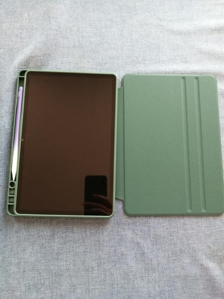 Tablette iPad avec son étui ouvert, laissant apparaître le stylet. L'étui est de couleur verte et la tablette est posée sur u...