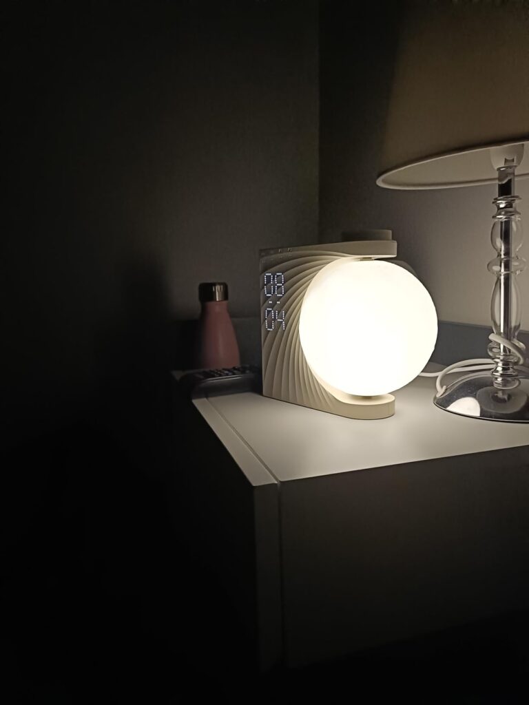 Le réveil-lumière en forme de lune dans une chambre, posé sur une table de chevet blanche. La lune est éclairée à pleine puis...