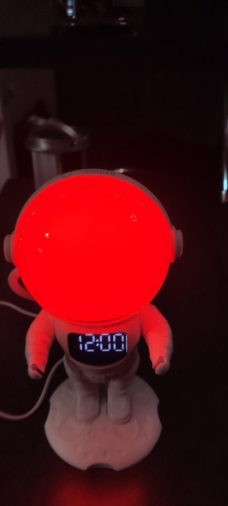 Le projecteur astronaute est allumé et émet une lumière rouge intense à travers sa visière. L'heure '12:00' est affichée sur...