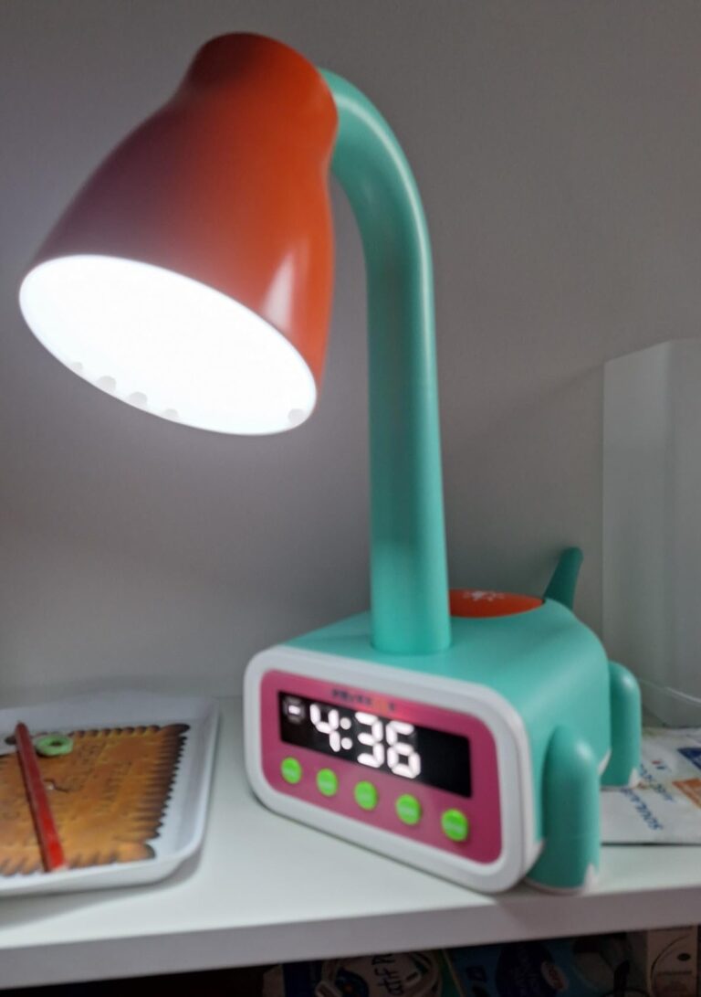 La lampe est posée sur une étagère. Son horloge indique 4h36. La lampe est allumée.