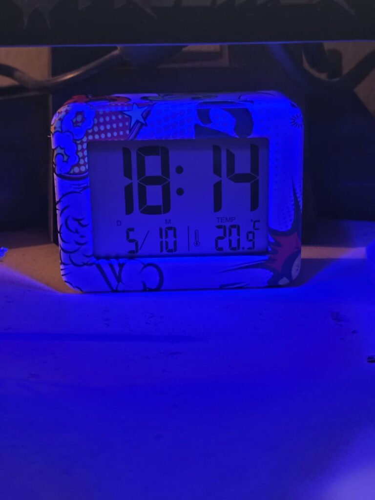 Un réveil numérique de couleur bleu, sur une table, affichant l'heure et la température. L'image est légèrement floue et somb...