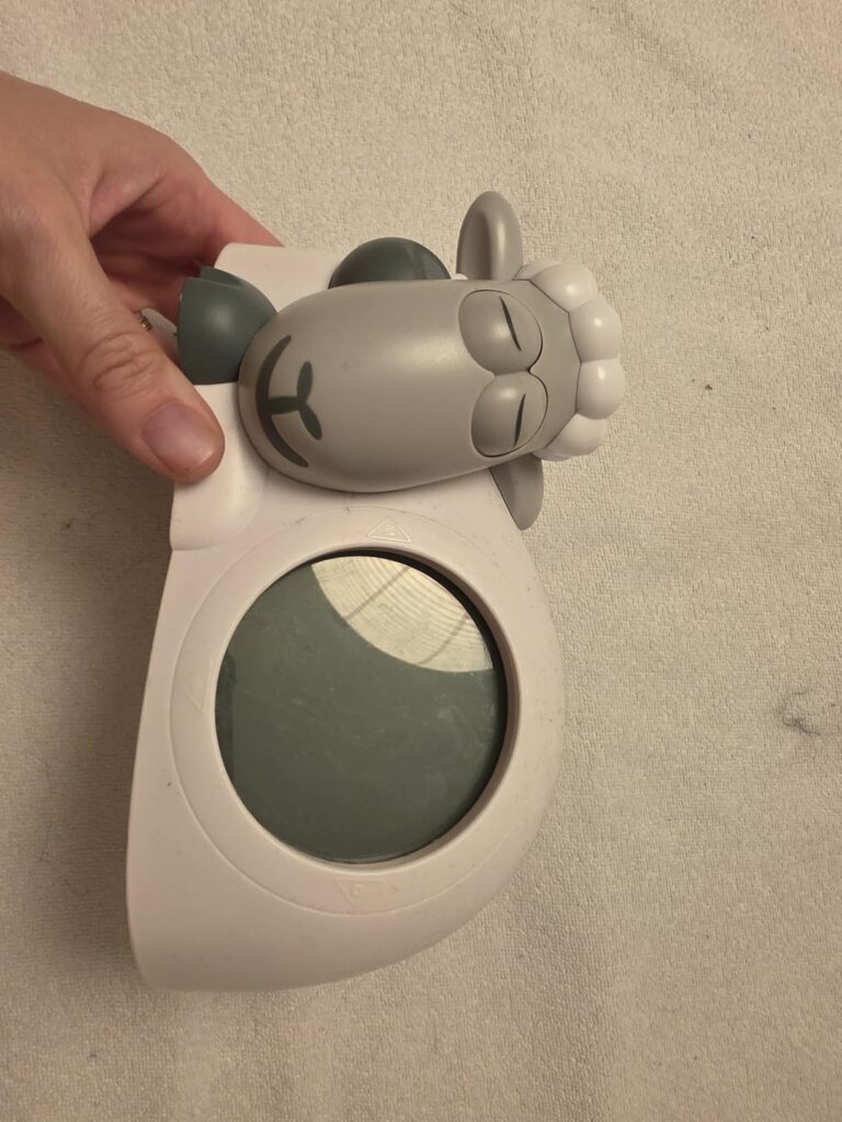 Réveil de jour pour enfant en forme de mouton, vu de face et sur le côté, tenu par la main. Le visuel 0 montre le même objet...