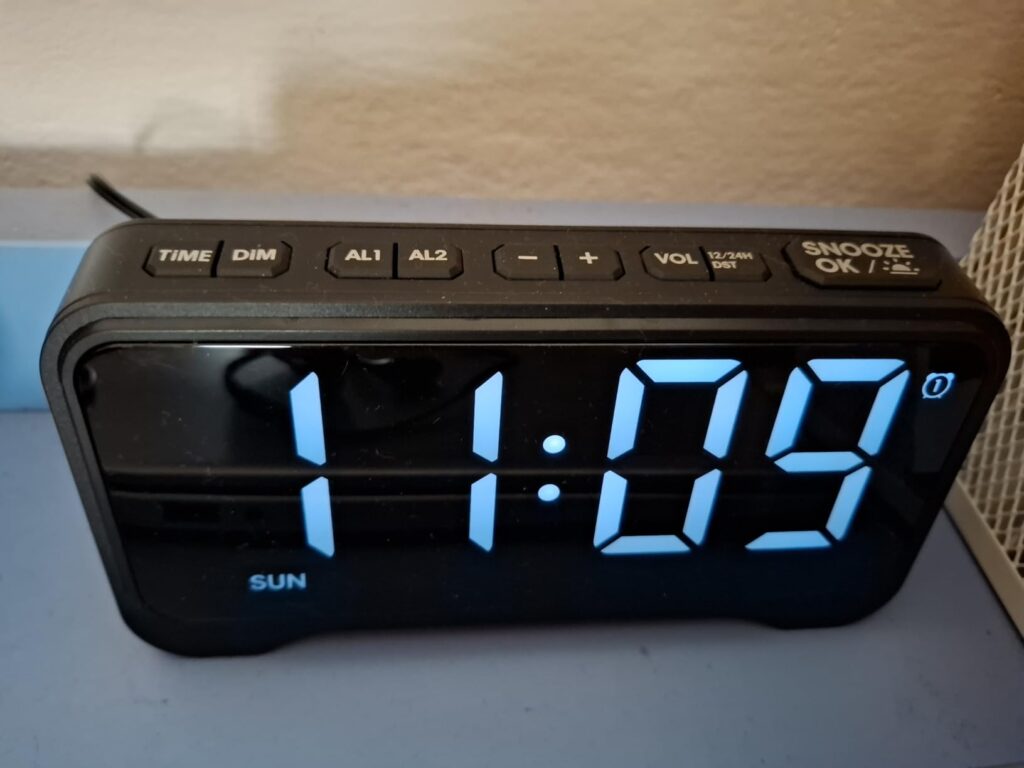Gros plan sur l'écran du réveil, avec les boutons du dessus. L'heure affichée est 11:09 avec la mention 'SUN' pour Dimanche.