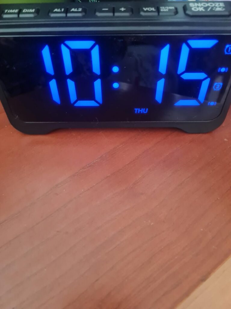 Gros plan sur l'écran du réveil. L'heure affichée est 10:15 avec la mention 'THU' pour Jeudi.