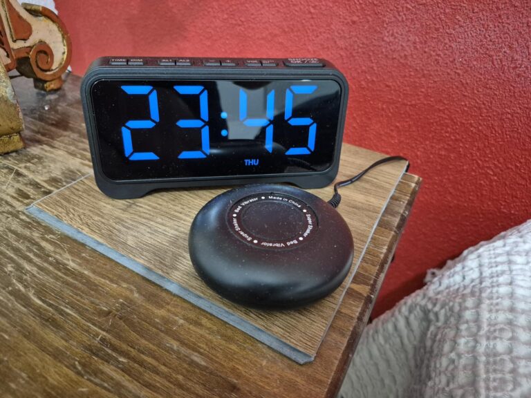 Le réveil sur une table de chevet, avec le vibreur branché. L'heure affichée est 23h45. Fond rouge.