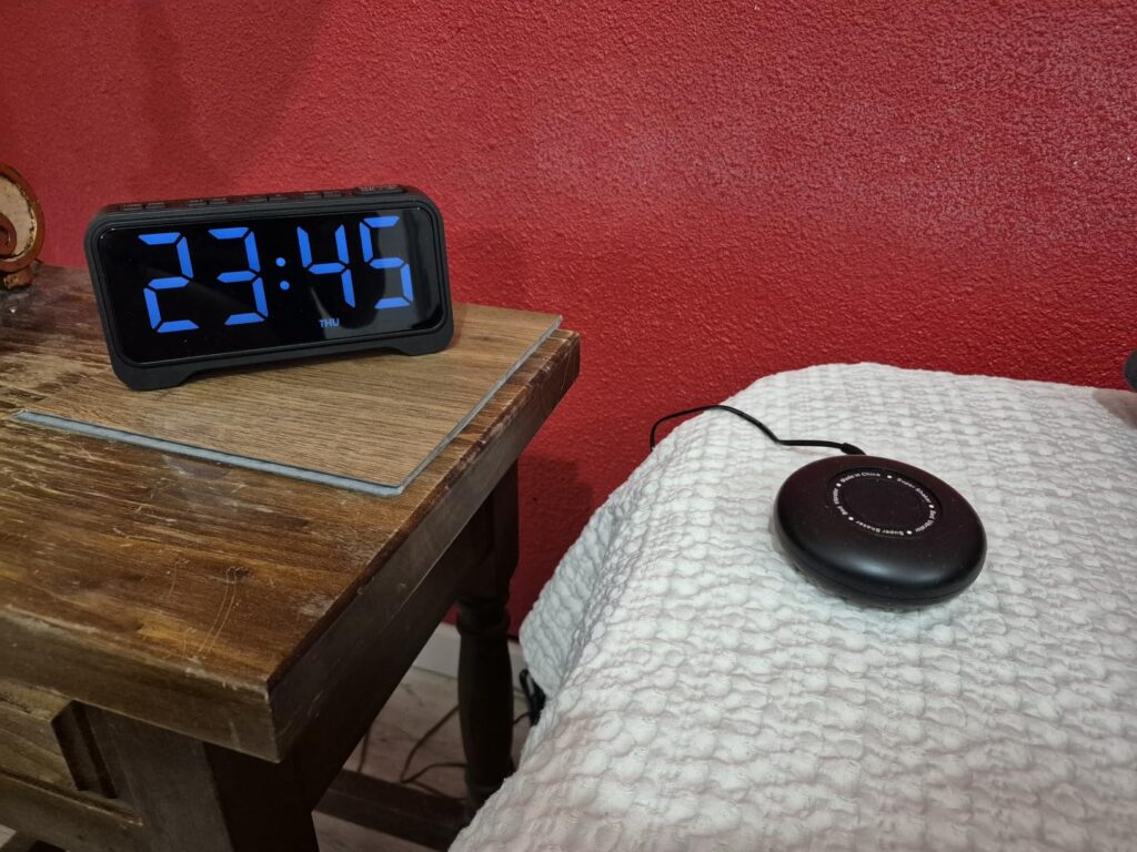 Le réveil sur une table de chevet, avec le vibreur sur le lit. L'heure affichée est 23h45. Fond rouge.