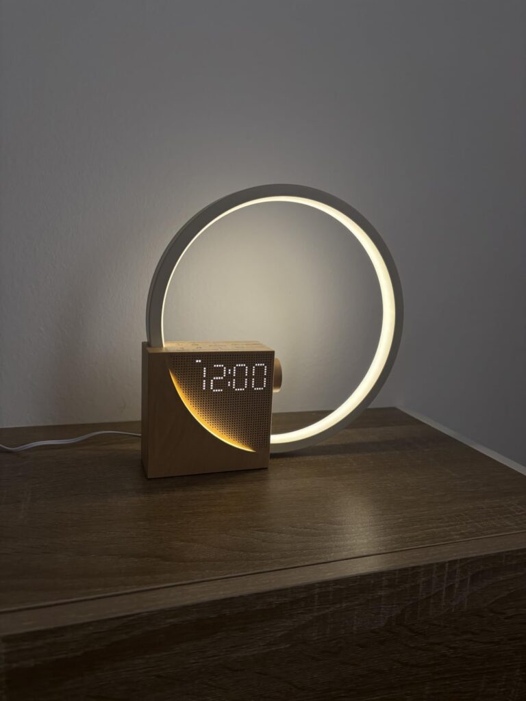 Réveil lumineux sur une table de chevet, allumé, heure affichée à 12h00.