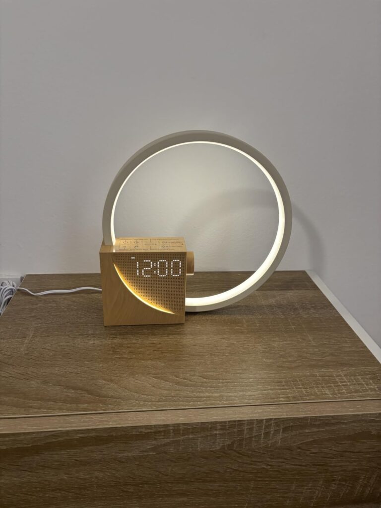Réveil lumineux sur une table de chevet, allumé, heure affichée à 12h00. Angle de vue légèrement différent de l'image précéde...