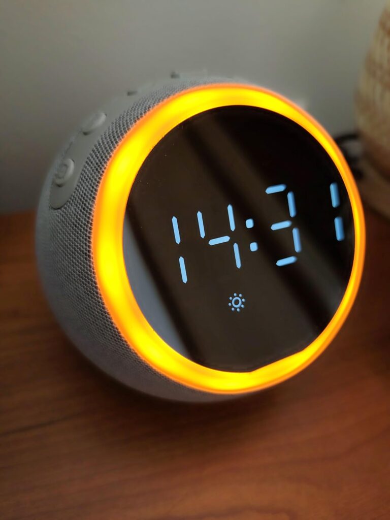 Réveil de forme sphérique avec affichage de l'heure 14:31 et un halo lumineux orange sur le pourtour, posé sur une table de c...