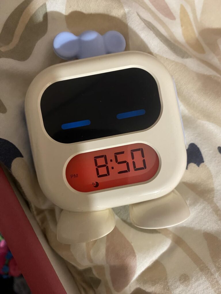 Réveil robot affichant 8h50 sur un lit. L'écran du haut est noir, l'écran du bas affiche l'heure en rouge.