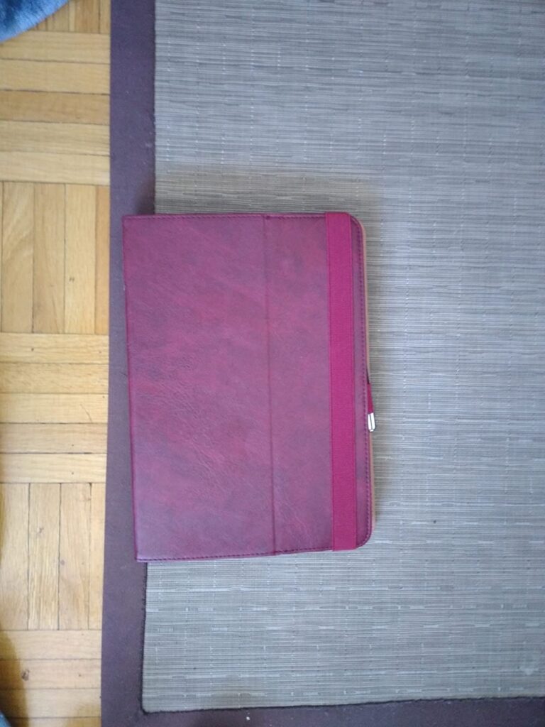 Coque de tablette de couleur bordeaux, vue de face, posée sur un tapis.