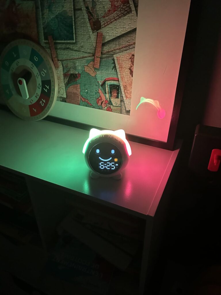 Réveil pour enfant blanc posé sur une table de chevet. Les oreilles de chat sont éclairées en vert et rouge. L'heure est affi...