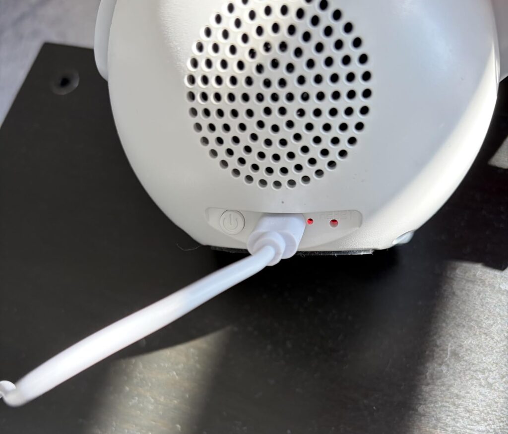 Détail de l'arrière du réveil, montrant la prise de chargement USB-C et le haut-parleur. Un câble blanc est connecté à la pri...