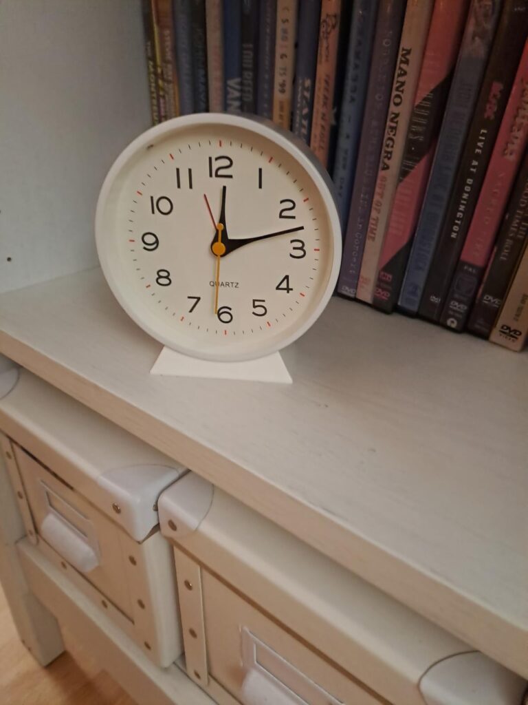 Un réveil rond blanc sur une commode blanche à côté d'une bibliothèque de livres
