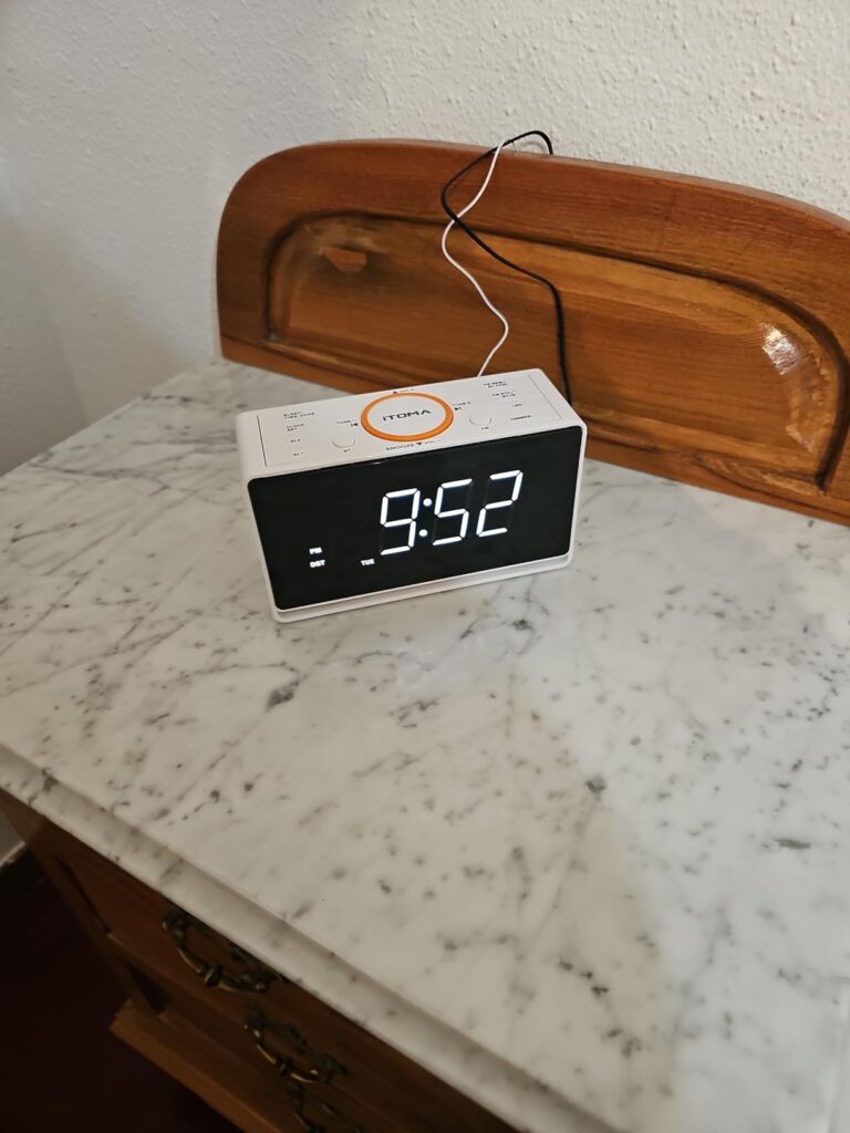 Vue de face du radio-réveil ITOMA posé sur une table de chevet. Il affiche l'heure 9:52.
