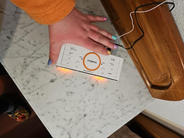 Vue de dessus du radio-réveil ITOMA posé sur une table de chevet, avec une main qui le manipule.