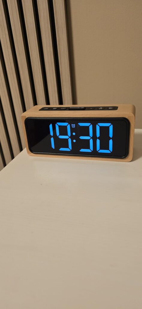 Réveil posé sur une table de chevet, affichant l'heure 19:30