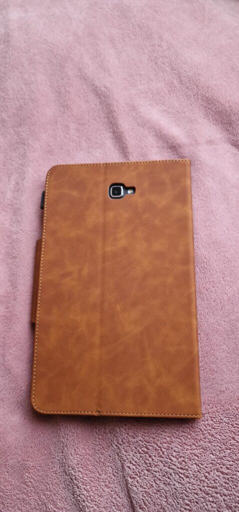 L'étui de protection marron clair avec la tablette insérée, vu de dos, posé sur une couverture violette. On voit l'emplacemen...