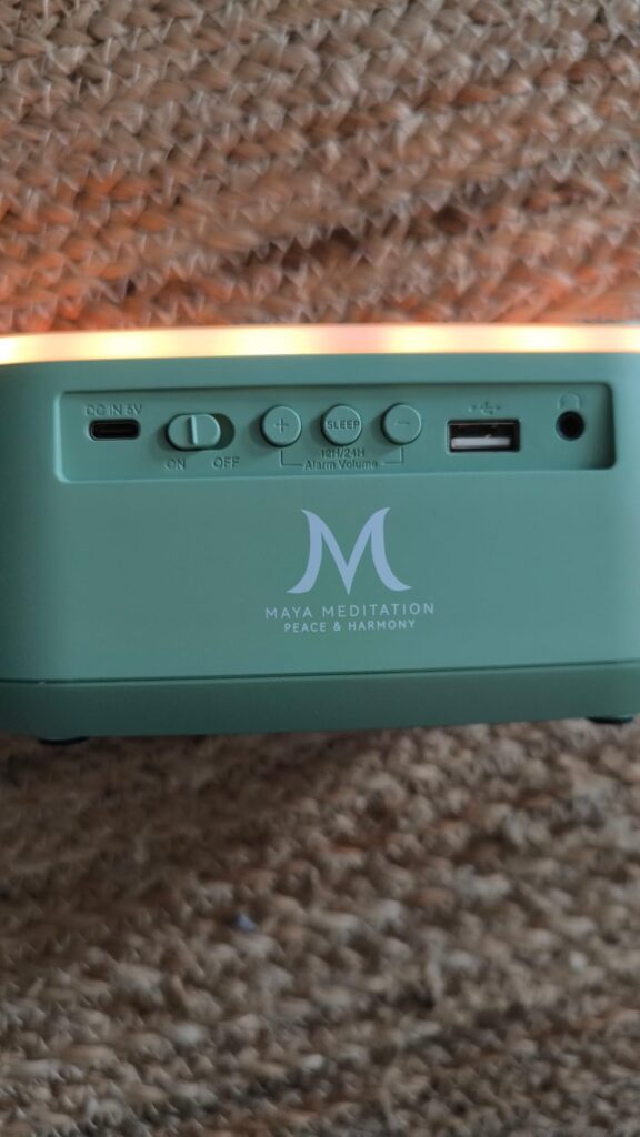 Gros plan sur l'arrière du réveil, montrant les ports (USB, carte SD, etc.) et le logo de la marque. Le rétroéclairage est bl...
