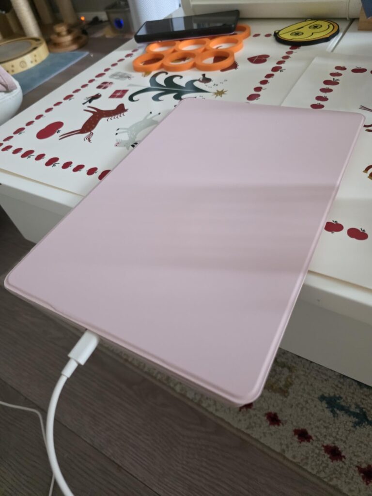 La tablette avec son étui de protection rose, posée sur une table, câble de chargement branché