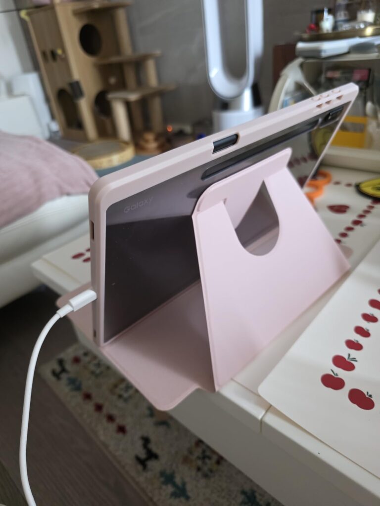 La tablette avec son étui de protection rose sur une table, déplié pour servir de support. Montre la même chose que l'image 1...
